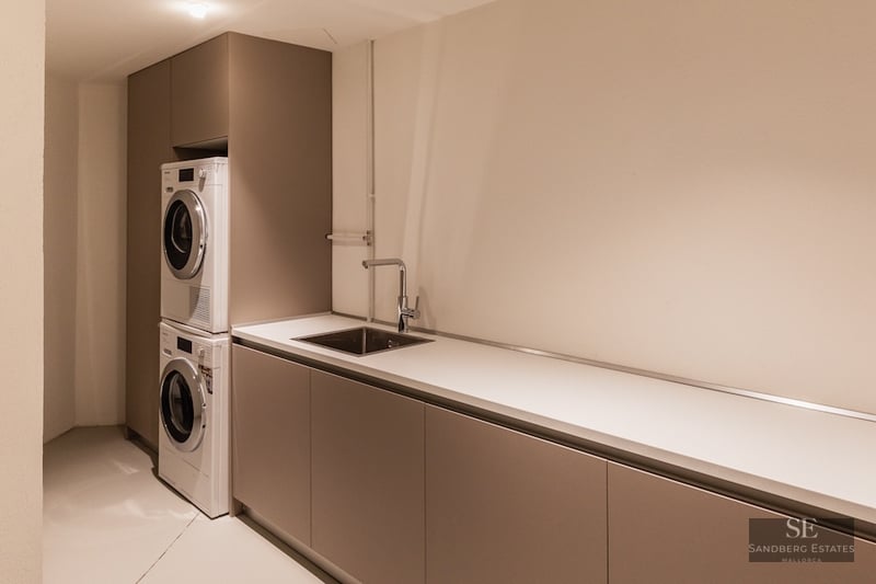 Modern laundry room with stacked washer and dryer, long white countertop, and integrated stainless steel sink.