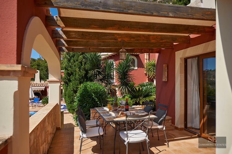 Covered terrace with a wooden pergola and dining table overlooking a tropical garden.