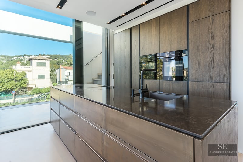 Modern kitchen featuring a large dark stone island, wood cabinetry, and floor-to-ceiling windows with a landscape view.