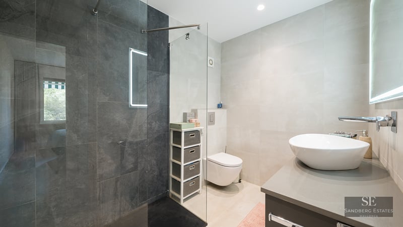 Salle de bain moderne avec douche en verre, carrelage gris foncé, vasque blanche et toilettes suspendues.