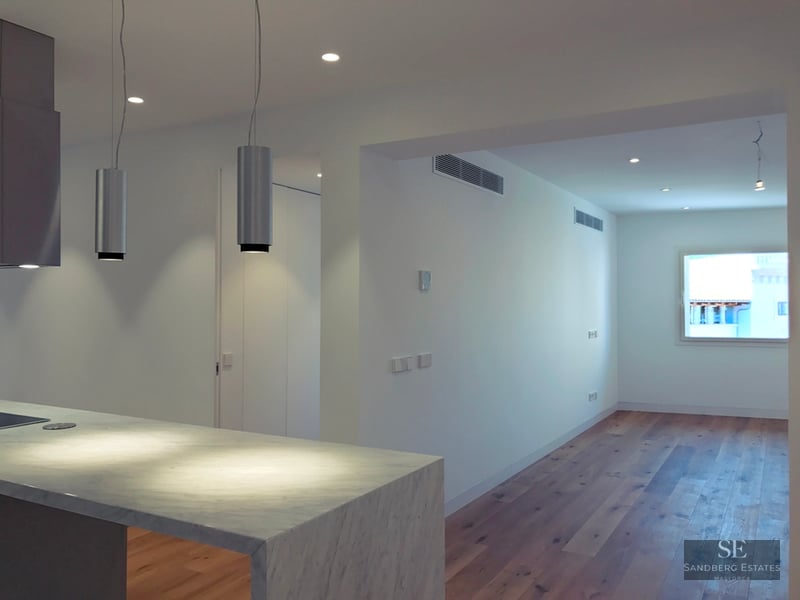 Modern kitchen featuring a white marble island and wood flooring leading into a bright living area.