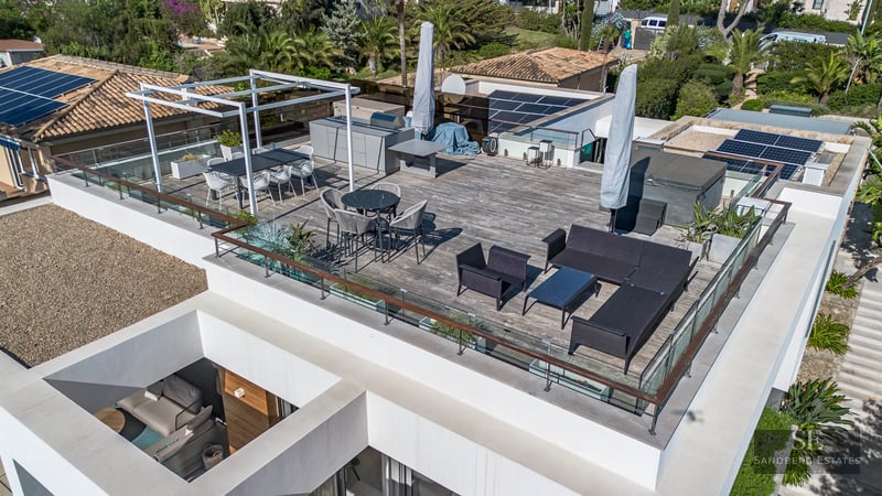 Vue aérienne d'une terrasse de toit moderne avec salon, espace repas, cuisine extérieure et garde-corps en verre.