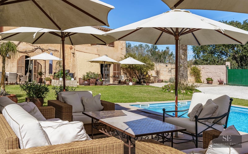 A luxury swimming pool surrounded by large white umbrellas and wicker lounge furniture in a Mediterranean garden.