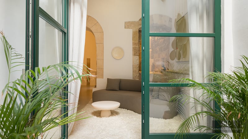 View through green glass doors into a modern living room with a stone arch, white rug, and brown sofa.