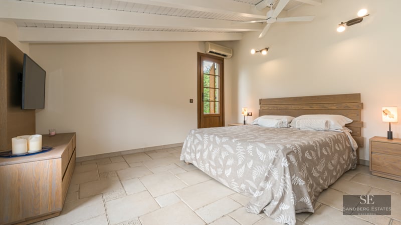 Bedroom featuring a wooden bed, white beamed ceiling, stone floors, and a glass door.