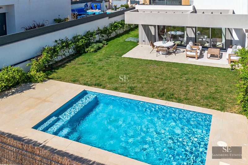 Exterior view of a modern villa with pool. Minimalist architecture, large windows, and lush landscaping. Clear blue sky.