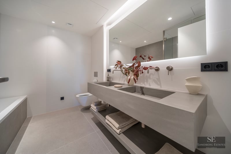 Minimalist bathroom featuring a floating grey concrete double vanity, large backlit mirror, and wall-mounted faucets.