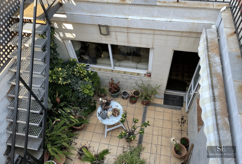 Overhead view of a tiled patio with a metal staircase, numerous potted plants, and a small white round table.