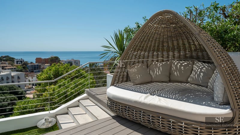 Pool view with loungers and umbrellas, surrounded by lush greenery and a modern house.