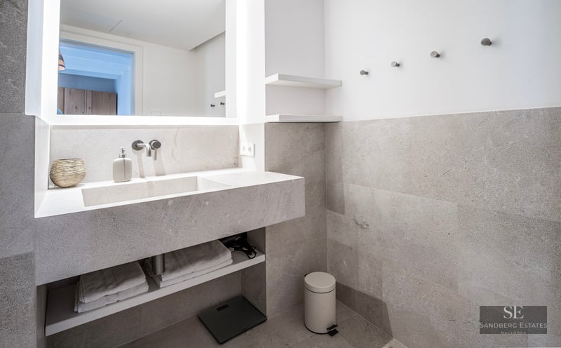 Salle de bain moderne avec vanité flottante en pierre grise, lavabo intégré et grand miroir rétroéclairé.