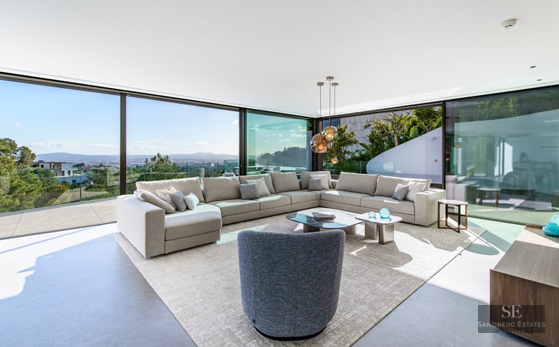 Modern bright living room with large grey sectional sofa and floor-to-ceiling windows overlooking a scenic valley.