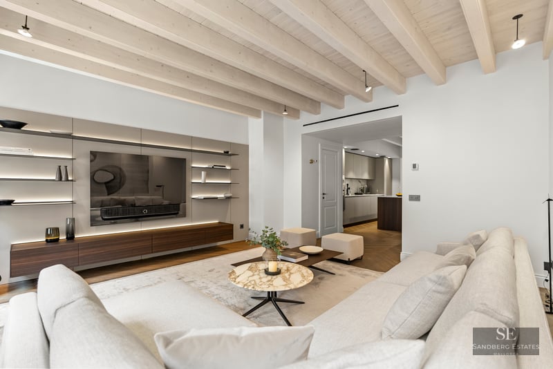 Modern living room with white sofas, marble coffee table, wood-beamed ceiling, and built-in TV wall.