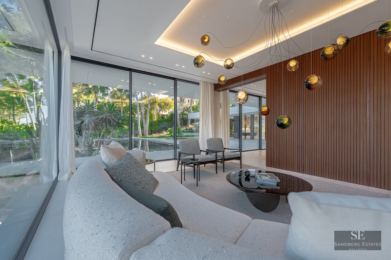 A contemporary living room featuring a curved sofa, designer lighting, and large windows overlooking a lush garden.