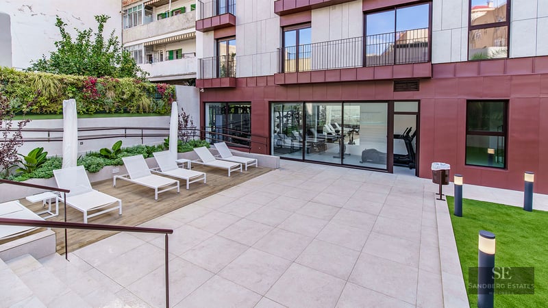 Modern outdoor terrace with white sun loungers, a vertical garden wall, and a view into a glass-walled gym.