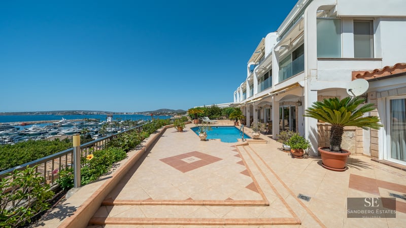 Expansive outdoor terrace with a swimming pool overlooking a marina with yachts under a clear blue sky.