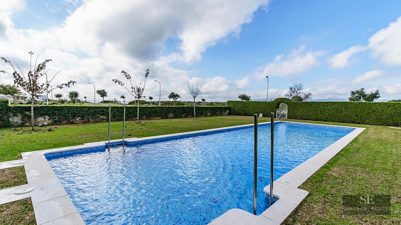 Large rectangular blue-tiled swimming pool surrounded by a green lawn and manicured hedges under a cloudy sky.