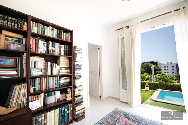 A room featuring a large dark wood bookshelf filled with books and an open door leading to an outdoor swimming pool.