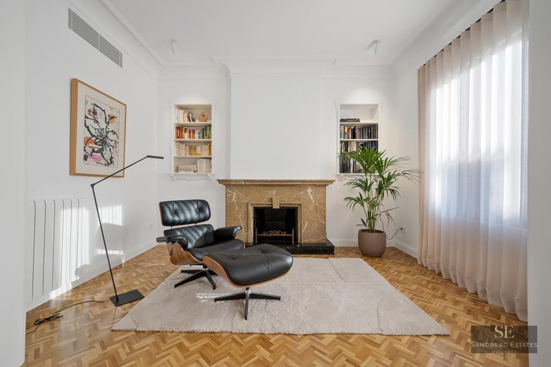 Modern living room with leather Eames chair, marble fireplace, parquet floor, and built-in bookshelves.