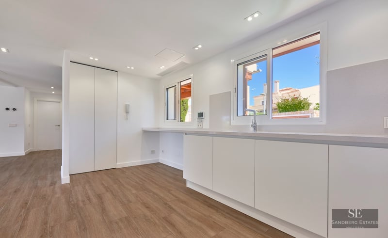 Modern kitchen with white cabinets, wood flooring, stainless steel sink, and bright windows.