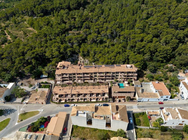 Bird's eye view of a multi-story terracotta-roofed apartment complex nestled against a lush green forest.