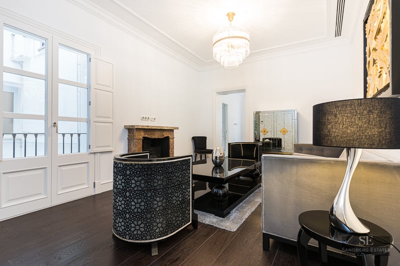 Elegant living room with white walls, dark wood floors, designer furniture, crystal chandelier, and a marble fireplace.