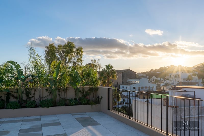 Terrasse de toit moderne avec carrelage en pierre et plantes tropicales, surplombant une ville méditerranéenne au coucher du soleil.