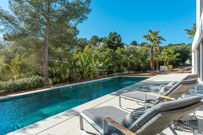 Vue aérienne d'un jardin luxuriant avec piscine entourée de gazon, d'arbres et d'une maison moderne avec de grandes baies vitrées.