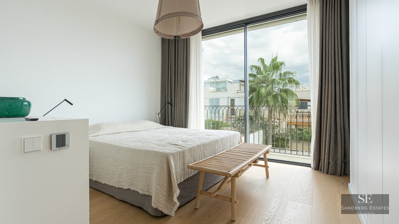 Bright bedroom with floor-to-ceiling windows, light wood floors, a large bed, and a palm tree view outside.