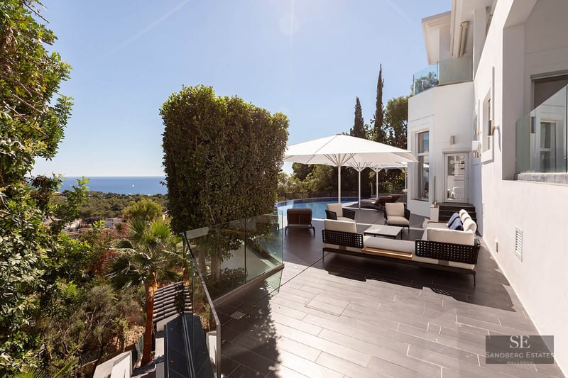 Modern terrace with designer lounge furniture, white umbrellas, and an infinity pool overlooking the sea.