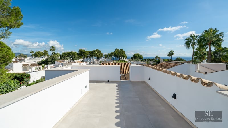 Spacious white rooftop with light stone tiling, offering panoramic views of palm trees, neighboring roofs, and the sea.