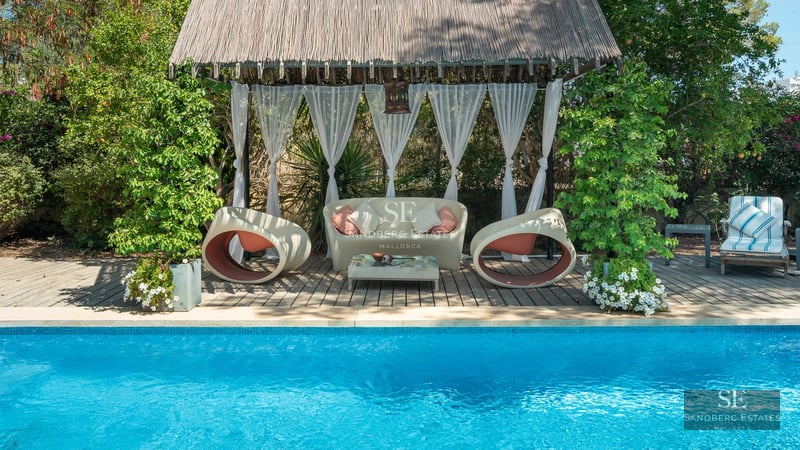 View of pool with sun loungers, lush garden, and modern facade. Minimalist architecture with large windows and neutral colors.