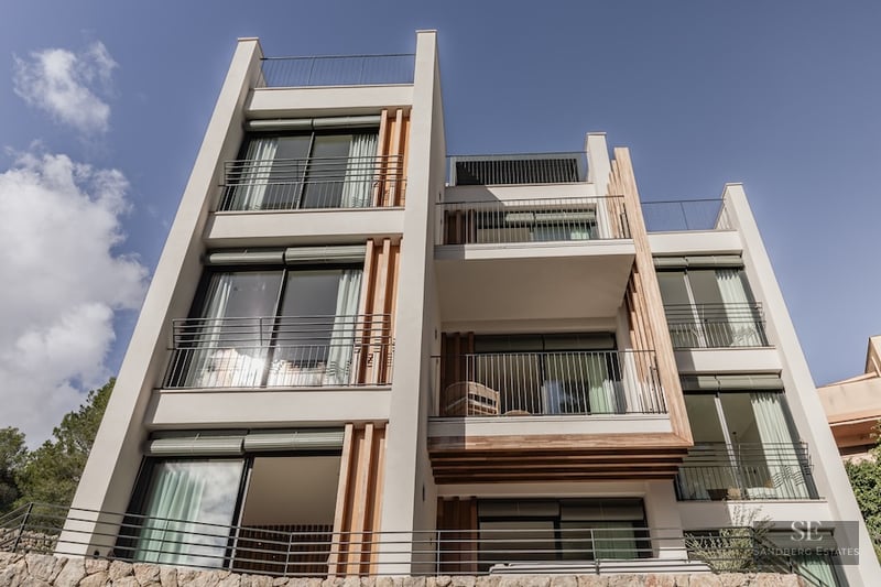 Low-angle view of a modern four-story villa with white walls, wooden slat accents, and glass balconies under a blue sky.