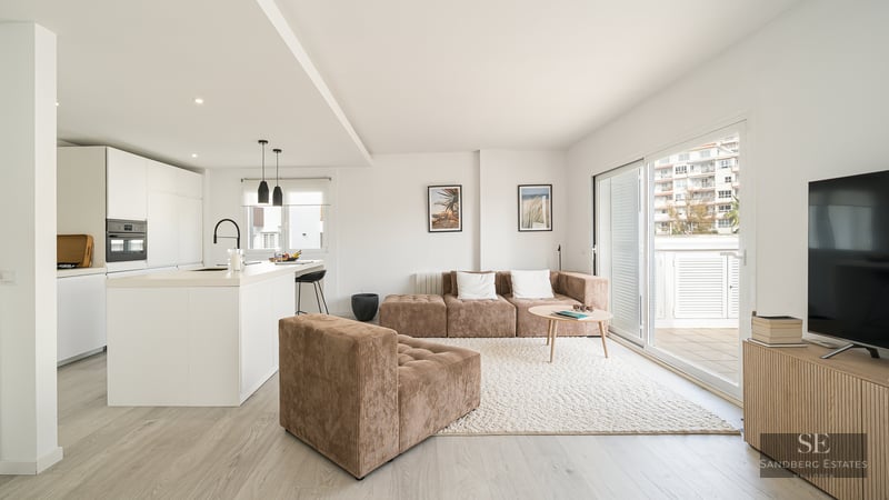Bright modern living room with a brown corduroy modular sofa, textured rug, and a minimalist white kitchen.