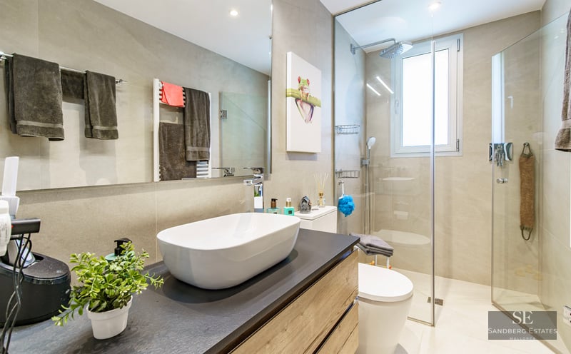 Modern bathroom featuring a white vessel sink on a dark vanity, glass-enclosed shower, and large mirror.