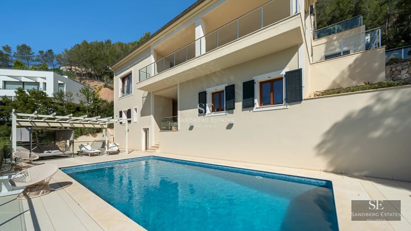 Exterior view of modern villa with pool, lush garden, and minimalist architecture. Large windows reflect the blue sky.