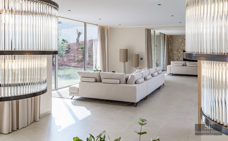 Spacious modern living room with cream sectional sofa, large glass walls viewing a garden, and stone accent wall.
