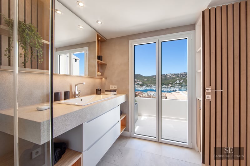 Modern bathroom with stone vanity, large mirror, and glass doors opening to a balcony with a marina view.