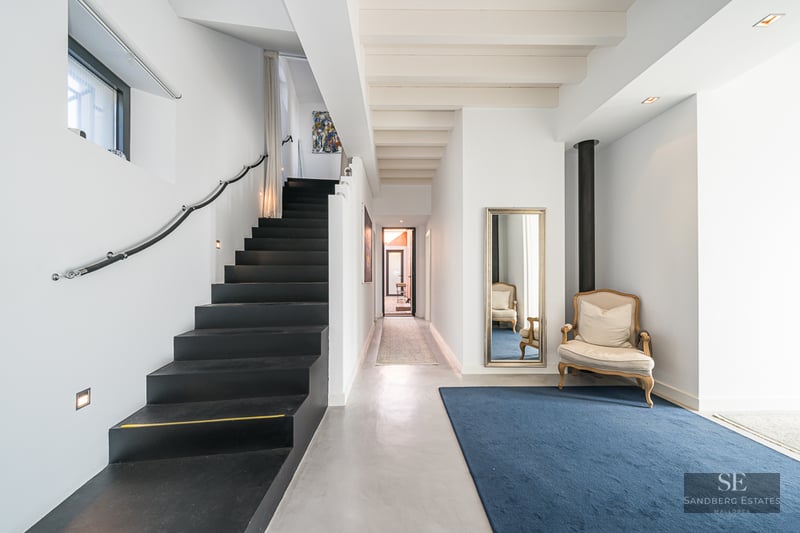 Modern entryway featuring a sleek black staircase, polished concrete floors, and a blue rug with a classic armchair.