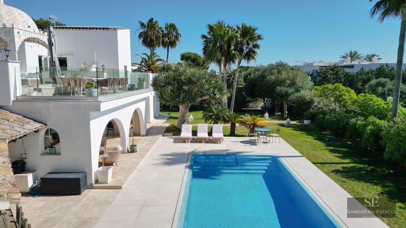 Modern white villa with rectangular blue pool, tropical garden, and glass-railed upper terrace.