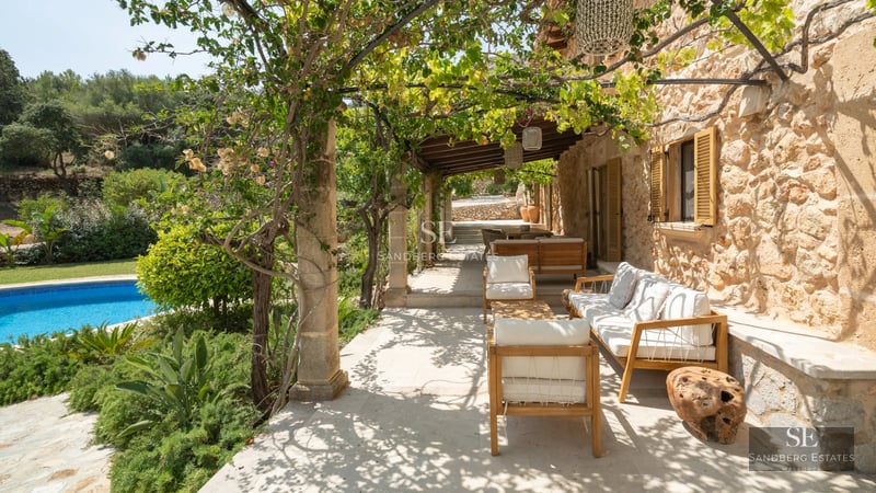 Large infinity pool bordered by a wooden deck and lush gardens. Modern facade with large windows.
