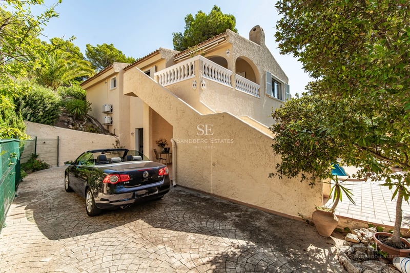 Panoramic view of an infinity pool with natural stone border. Lush garden and modern architecture. Bright blue sky.