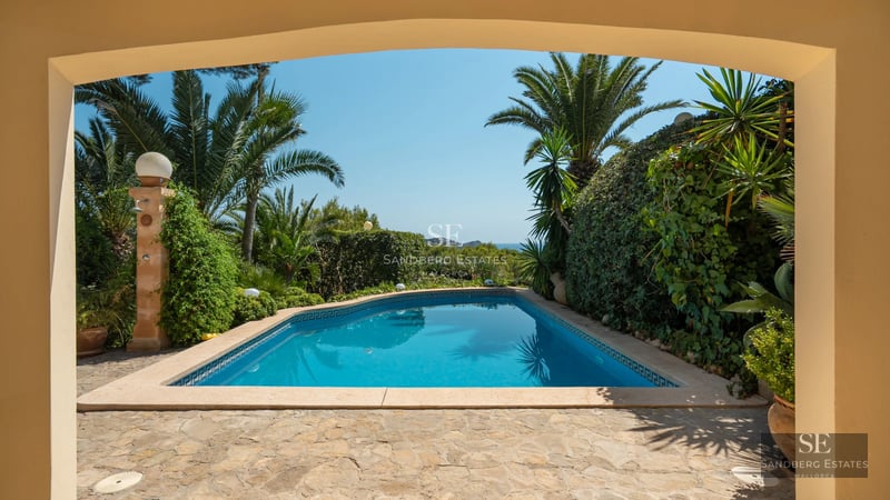 Exterior view of a modern villa with a swimming pool, garden and large windows reflecting natural light.