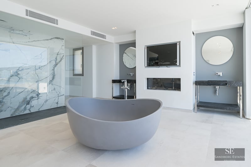 Modern bathroom featuring a grey freestanding tub, marble-walled shower, and dual vanities with round mirrors.