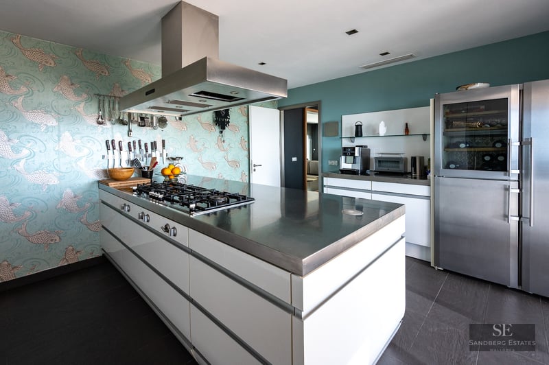 A luxury kitchen featuring a central stainless steel island, fish-patterned wallpaper, and high-end appliances.
