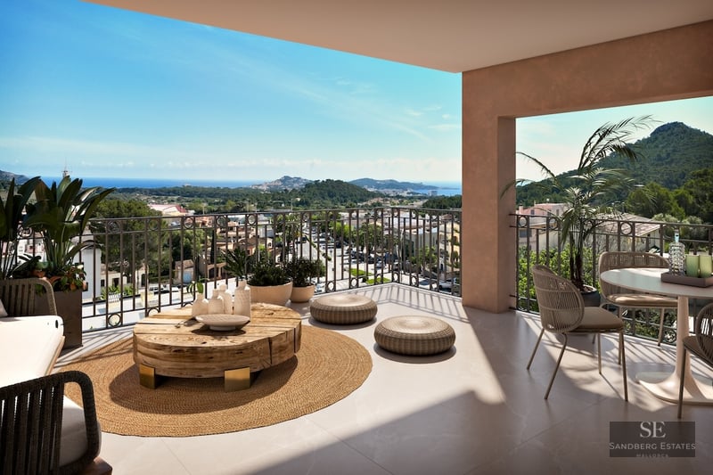 Spacious modern terrace with organic wood furniture and a jute rug overlooking a Mediterranean coastal town and sea.
