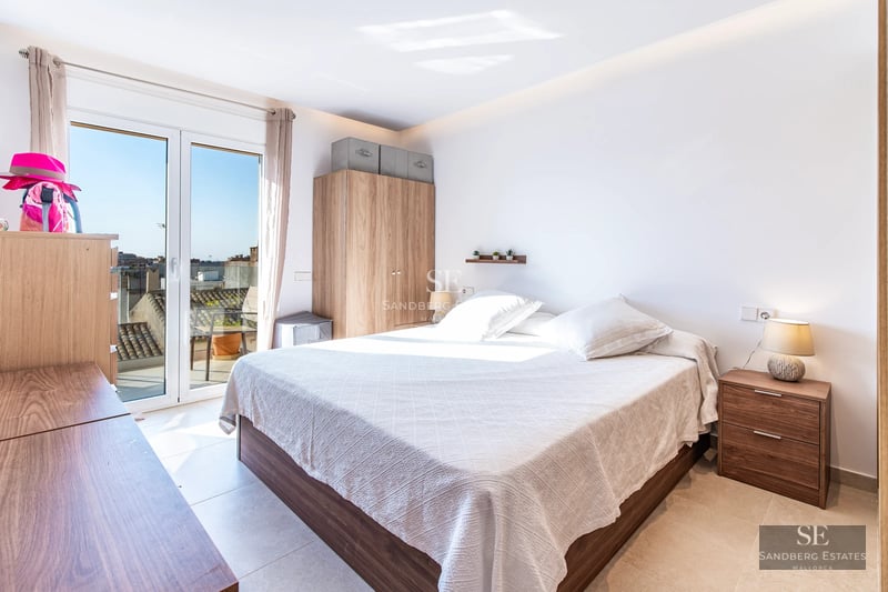 Spacious balcony with sea views, modern furniture, glass railing, wooden floor and lush vegetation.