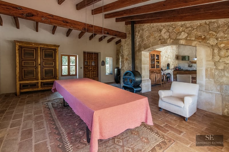 Large table with a pink cloth in a rustic room featuring wooden beams, stone walls, and a wood-burning stove.