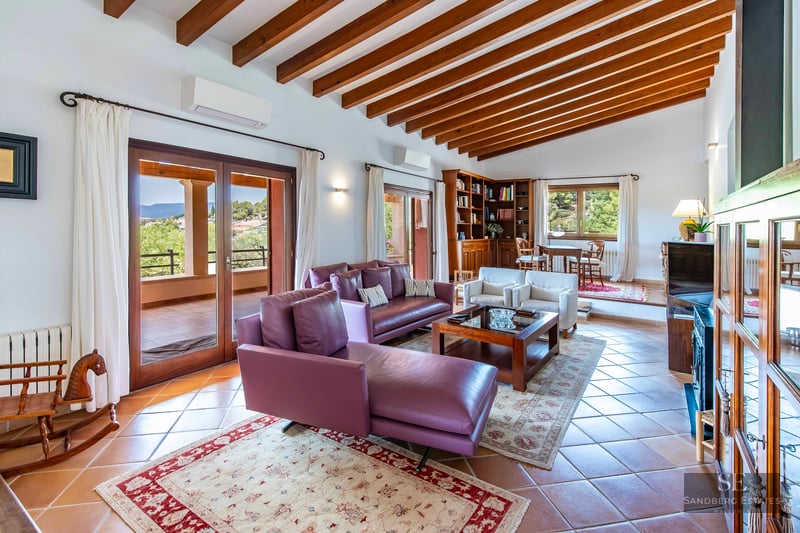 Bright living room with purple leather sofas, wooden ceiling beams, terracotta tiles, and terrace views.
