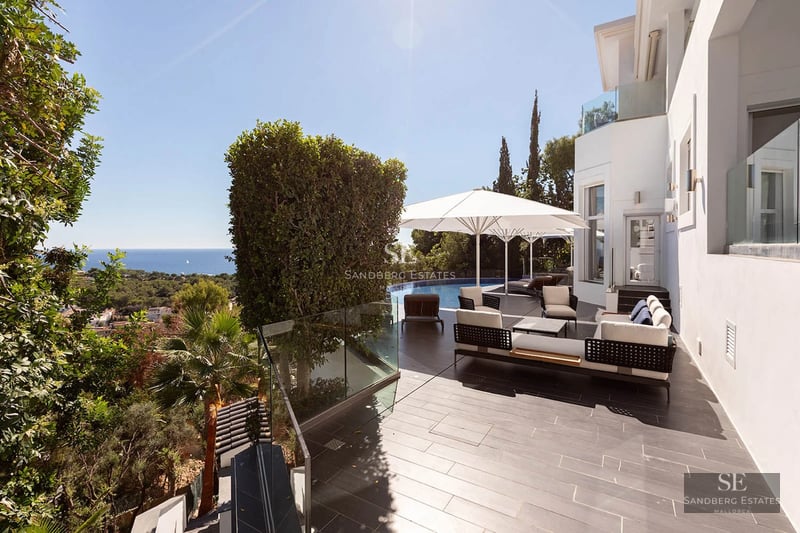 Spacious modern white villa terrace with designer outdoor furniture, an infinity pool, and panoramic ocean views.