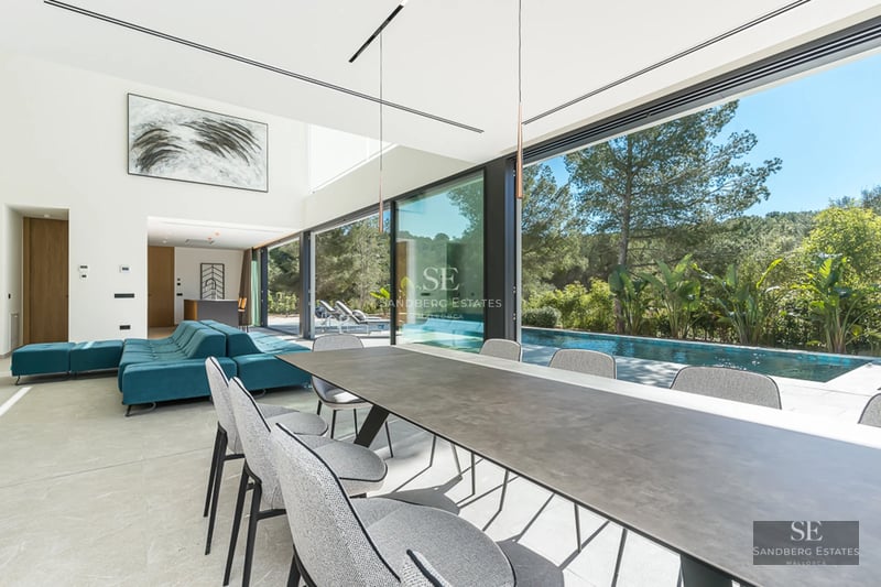 Vue extérieure d'une villa moderne avec piscine à débordement, chaises longues, pelouse et vue panoramique. Architecture minimaliste avec de grandes baies vitrées.